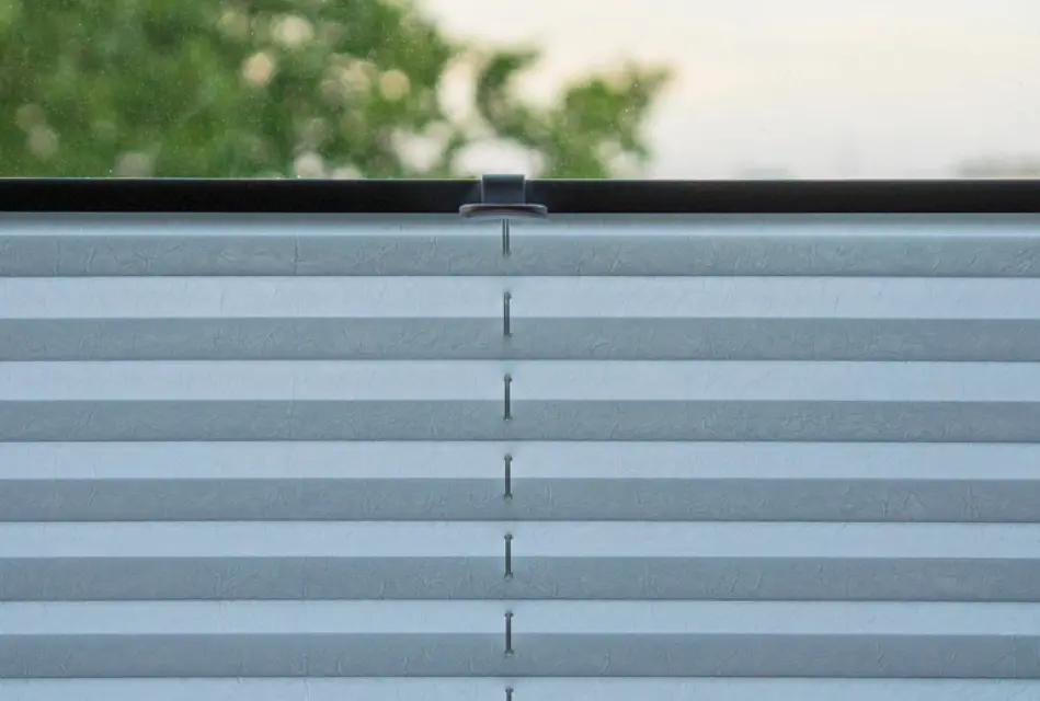 Detailaufnahme eines weißen Plissees am Fenster mit gleichmäßigen Falten. Moderner Sichtschutz und Sonnenschutz für Fenster in Wohnräumen mit stilvoller Fensterdekoration